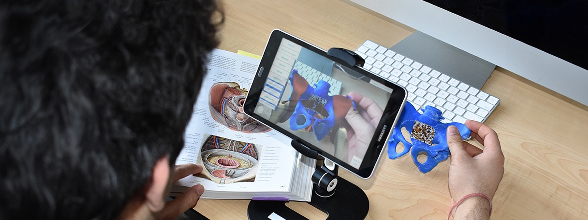 Student taking a photo of a pelvis bone and comparing it to a photo of the same bone in a medical textbook.